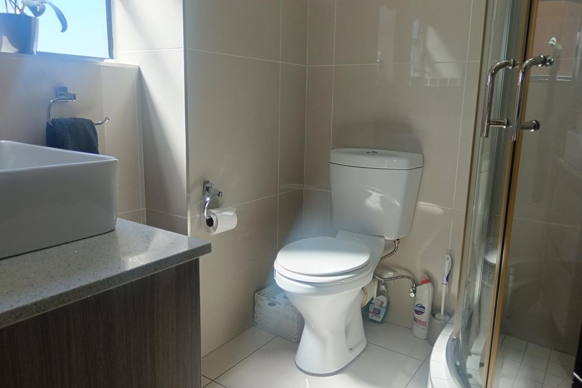 Modern bathroom featuring a vessel sink on a stone vanity, a standard toilet, and a glass-enclosed shower with neutral wall and floor tiling.