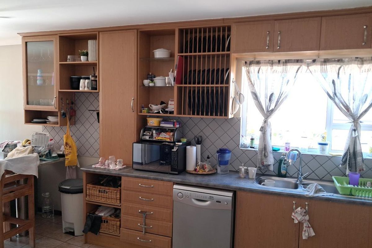 A functional kitchen featuring wood-look laminate cabinetry, tiled backsplash, and a double basin sink with a window view.