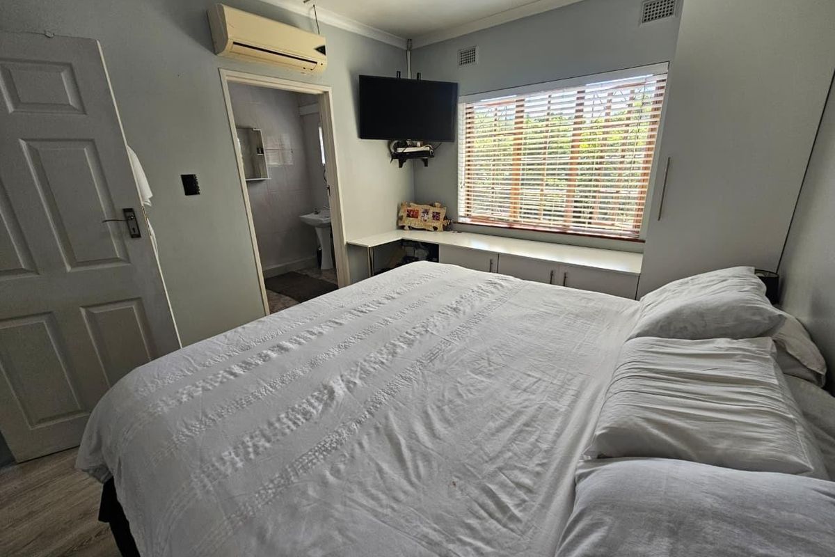 A functional bedroom featuring built-in cabinetry, laminate flooring, a wall-mounted air conditioning unit, and direct access to an en-suite bathroom.