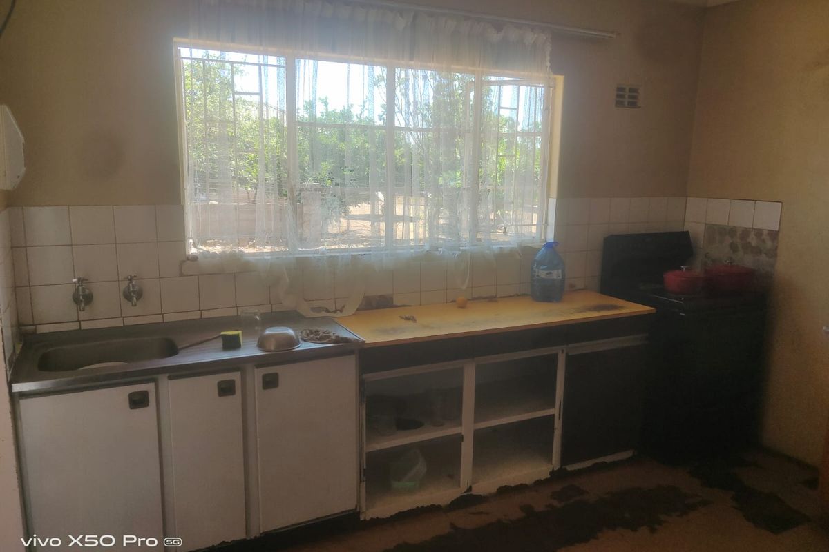 A dated kitchen featuring a stainless steel sink, tiled splashback, and built-in cabinetry requiring significant renovation and cosmetic updates.