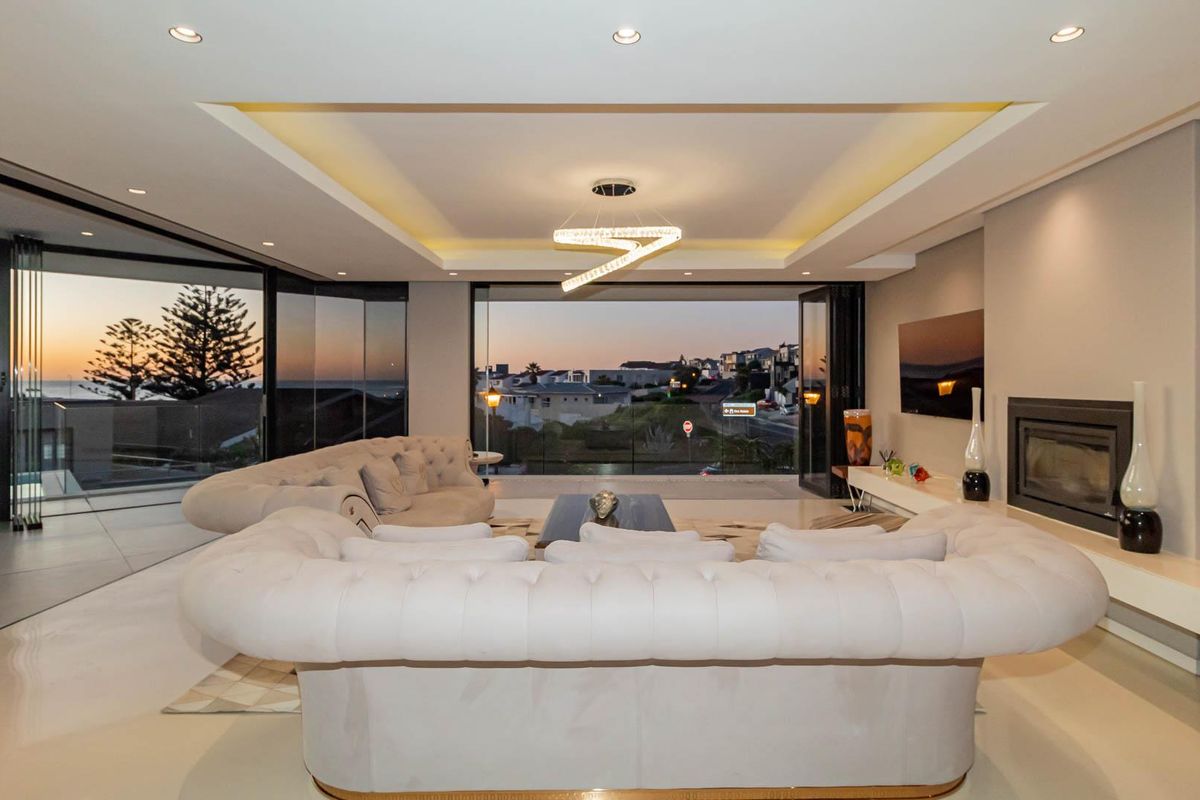 Spacious modern living room featuring a built-in fireplace, recessed tray ceiling with ambient lighting, and large sliding glass doors opening to a scenic view.