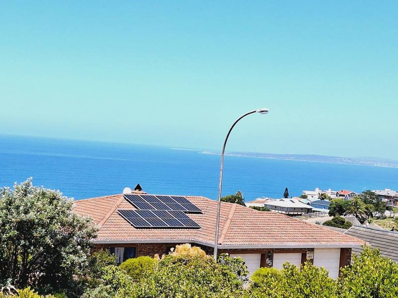 Elevated view of a residential property featuring a tiled roof with solar panels, overlooking the ocean and surrounding coastal neighborhood.