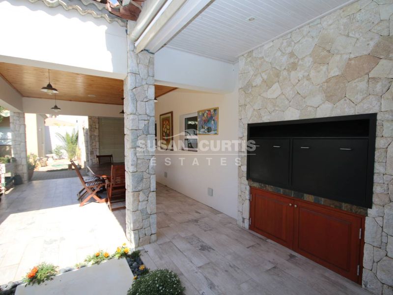 Spacious covered patio featuring stone cladding, a built-in braai, timber ceiling details, and tiled flooring, perfect for outdoor entertaining.