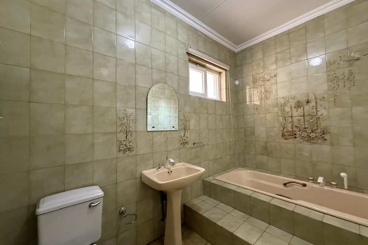 A dated bathroom featuring a pedestal basin, built-in bathtub with tiled surround, and full-height wall tiling.