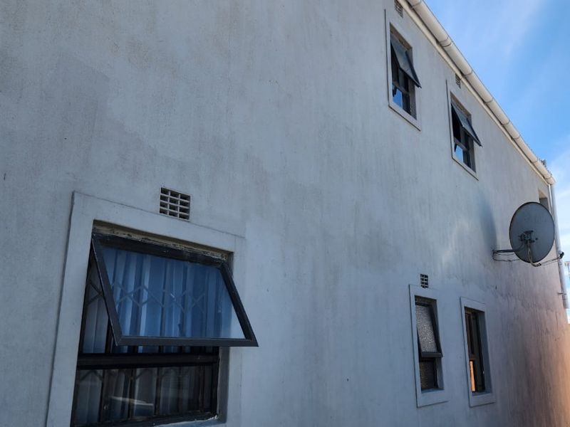 Side elevation of the property featuring multiple top-hung windows with security bars, gutters, and a mounted satellite dish.