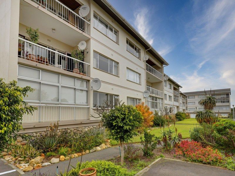Exterior view of the apartment building featuring multiple levels of balconies, large windows, and a well-maintained communal garden area.