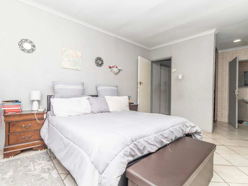 A bedroom featuring tiled flooring and an en-suite bathroom, showing signs of wear including visible wall cracks and paint deterioration.