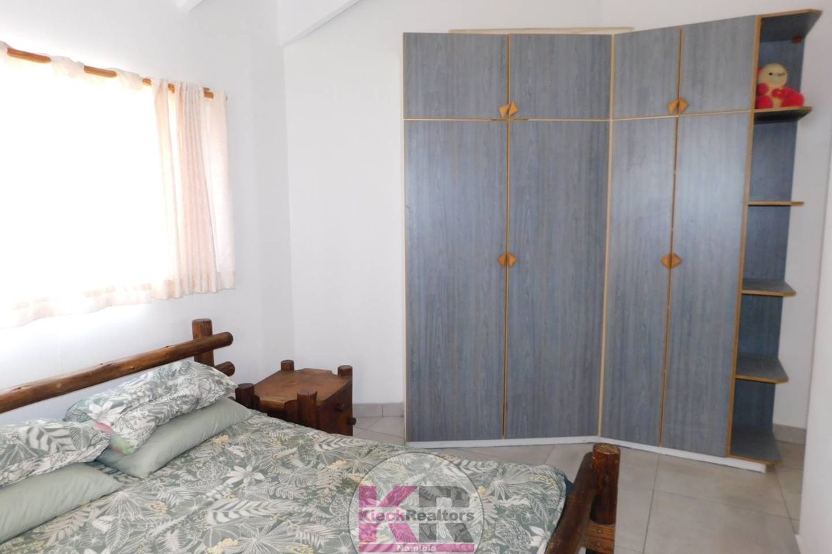 A bedroom featuring a built-in wardrobe, tiled flooring, and a vaulted ceiling, providing a functional and well-lit sleeping space.