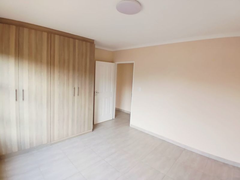 A clean, empty bedroom featuring neutral tiled flooring and ample built-in wooden cupboards, providing a versatile space ready for personalization.