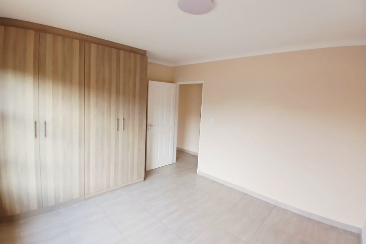 A clean, empty bedroom featuring neutral tiled flooring and ample built-in wooden cupboards, providing a versatile space ready for personalization.