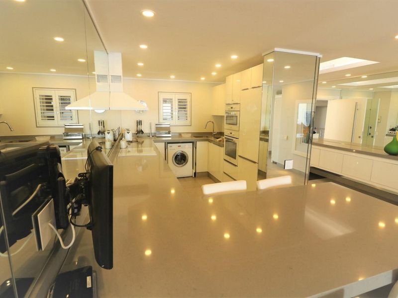 Modern kitchen featuring sleek stone countertops, integrated appliances, built-in oven and microwave, and stylish mirrored wall accents with recessed lighting.