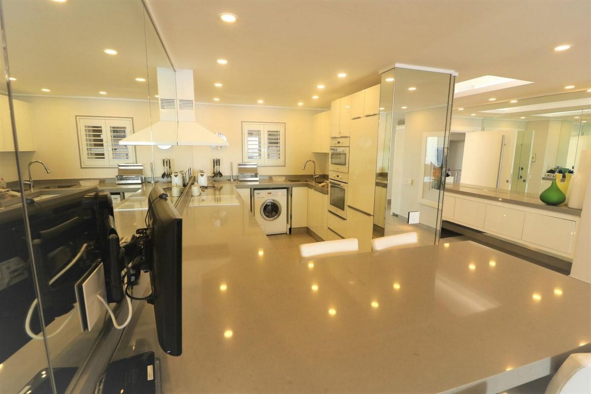 Modern kitchen featuring sleek stone countertops, integrated appliances, built-in oven and microwave, and stylish mirrored wall accents with recessed lighting.