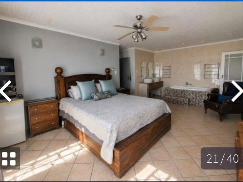 Spacious open-plan bedroom featuring an integrated en-suite bathroom area with a built-in bathtub and double vanity, finished with tiled flooring and a beadboard ceiling.