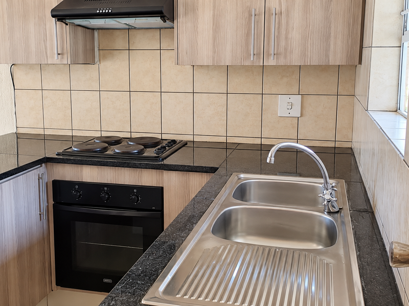 A clean, functional kitchen featuring laminate cabinetry, granite countertops, a built-in oven, electric hob, and a stainless steel double sink with tiled backsplash.