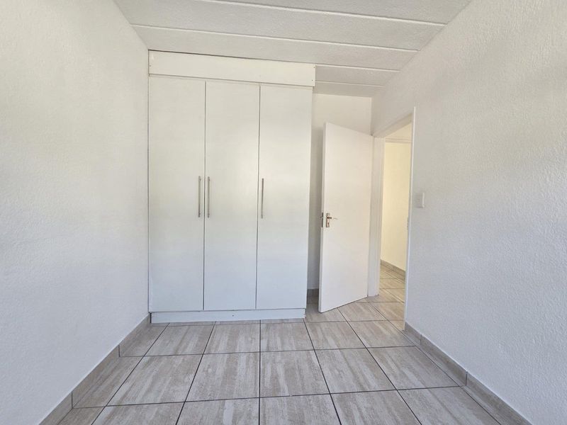 A clean, empty bedroom featuring neutral tiled flooring, a built-in white wardrobe, and a drop ceiling, offering a blank canvas for personalization.