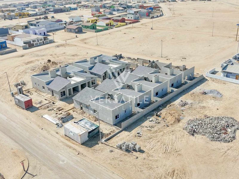 Aerial view of a townhouse development under construction, featuring multiple units with tiled roofs and perimeter walls in a developing residential area.