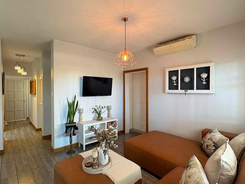 A well-maintained living room featuring tiled flooring, a wall-mounted air conditioning unit, and a modern pendant light fixture.