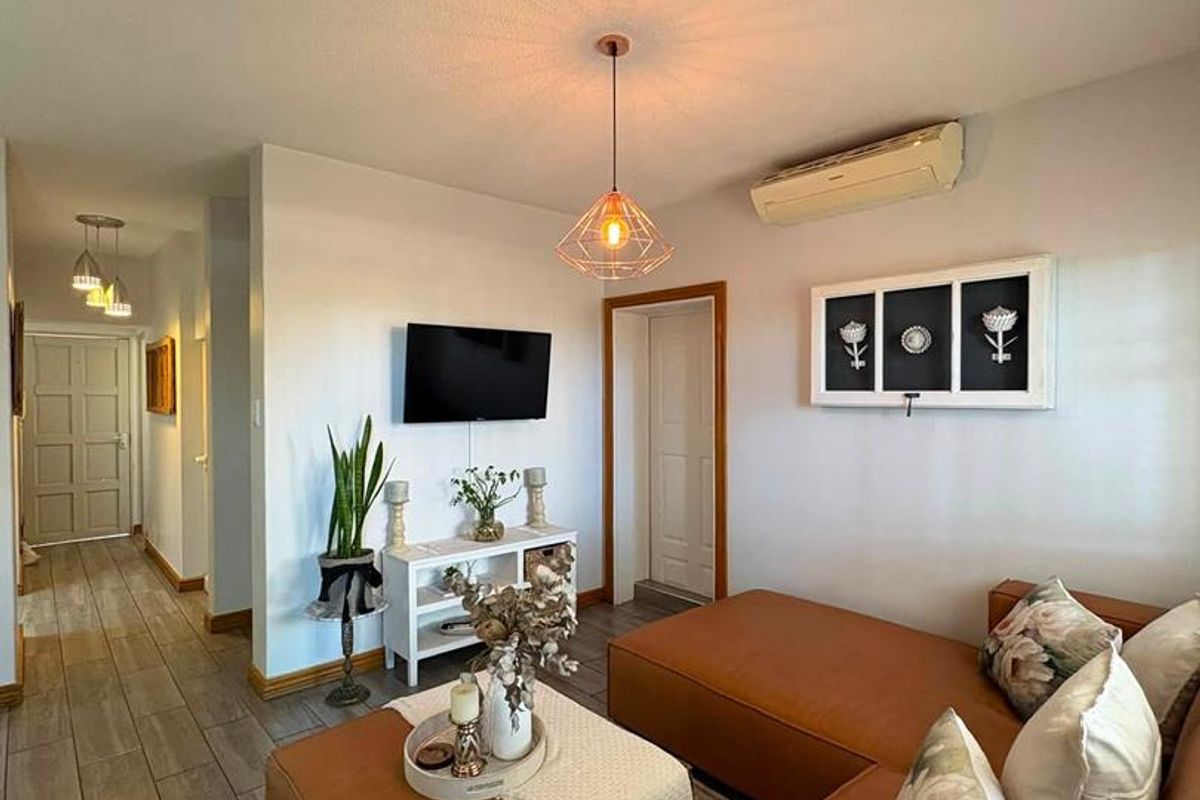 A well-maintained living room featuring tiled flooring, a wall-mounted air conditioning unit, and a modern pendant light fixture.