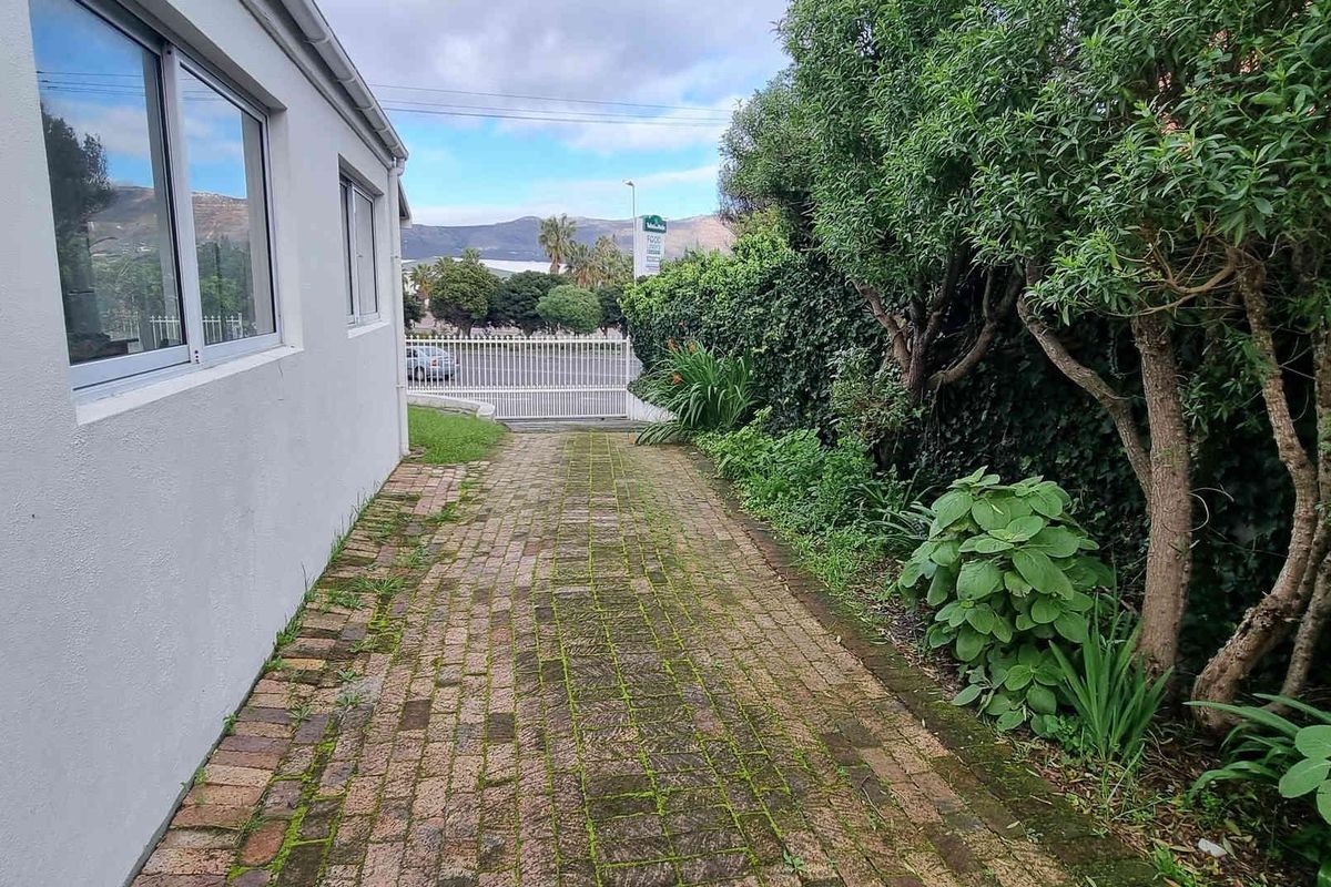 A side pathway featuring brick paving with established garden borders and a metal security gate leading to the street.
