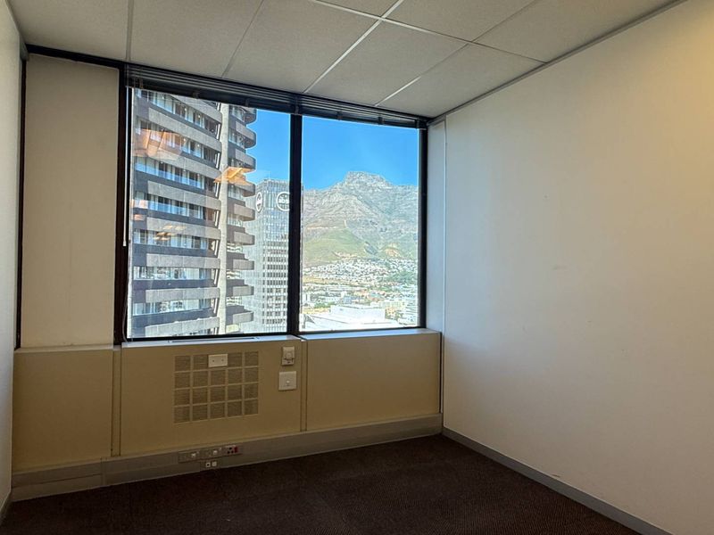 A vacant office space featuring a large window with city and mountain views, suspended ceiling, and integrated HVAC unit.