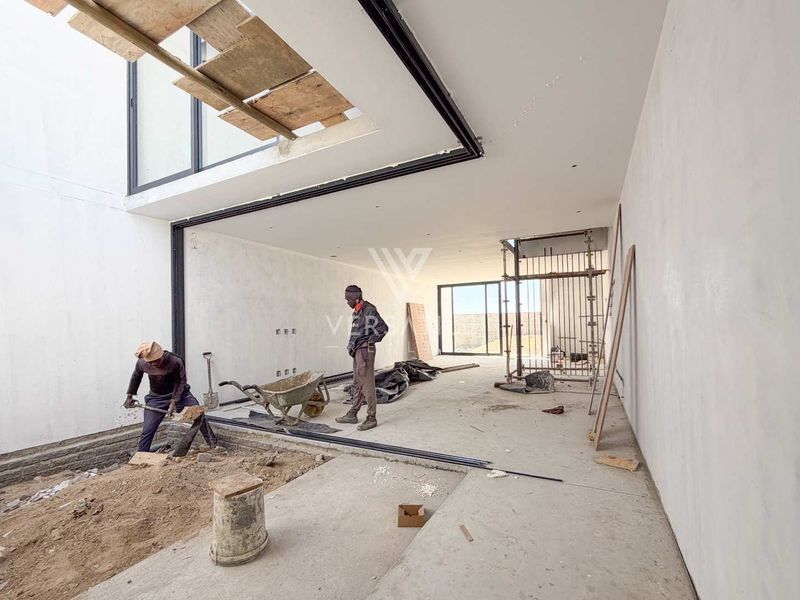 An open-plan living area currently under construction, featuring large sliding glass doors and recessed lighting, awaiting final flooring and interior finishes.