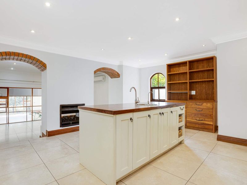 Spacious kitchen featuring a central island with wooden countertop, built-in cabinetry, shelving, and elegant archway details, finished with neutral tiled flooring.