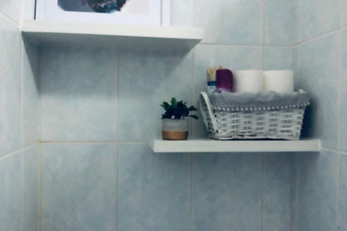 A compact bathroom corner featuring light blue wall tiles and two built-in floating shelves for storage.