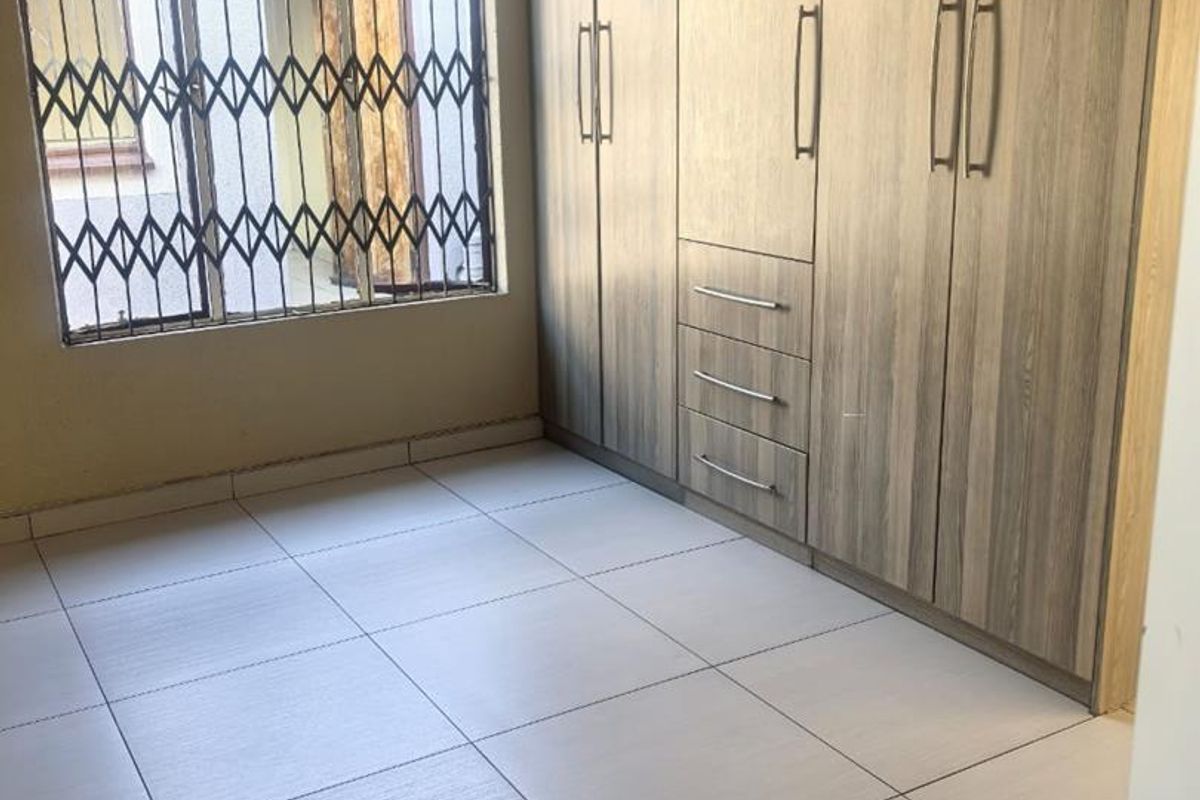 A clean, empty bedroom featuring neutral tiled flooring and extensive built-in wooden cupboards, providing ample storage space.
