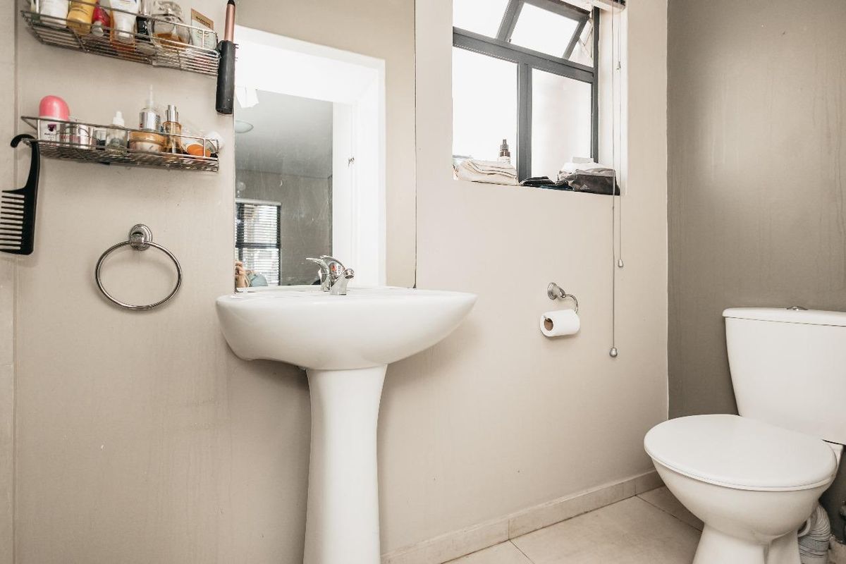 A functional bathroom featuring a white pedestal basin, a standard toilet, tiled flooring, and a window for natural light.