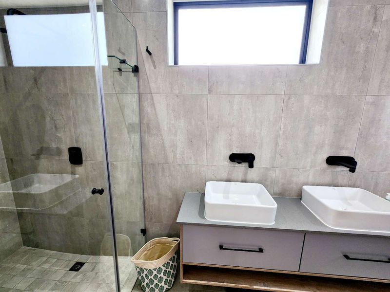 Modern bathroom featuring a double vanity with vessel sinks, wall-mounted matte black faucets, and a spacious walk-in shower with a glass enclosure.