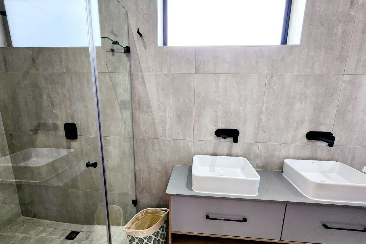 Modern bathroom featuring a double vanity with vessel sinks, wall-mounted matte black faucets, and a spacious walk-in shower with a glass enclosure.