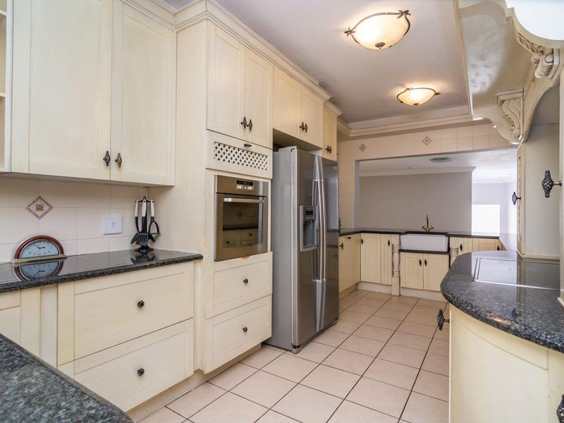 A traditional kitchen featuring cream cabinetry, dark granite countertops, a farmhouse-style sink, and built-in oven, with tiled flooring throughout.