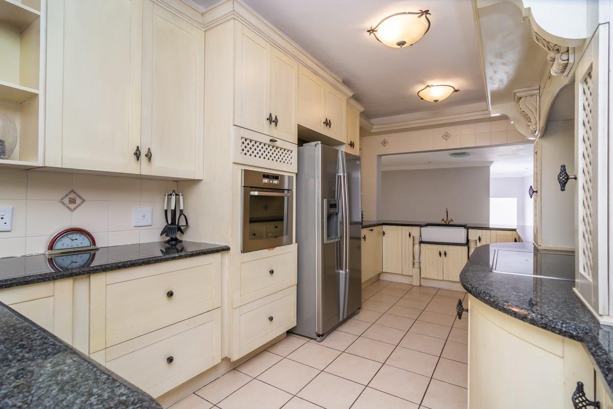 A traditional kitchen featuring cream cabinetry, dark granite countertops, a farmhouse-style sink, and built-in oven, with tiled flooring throughout.