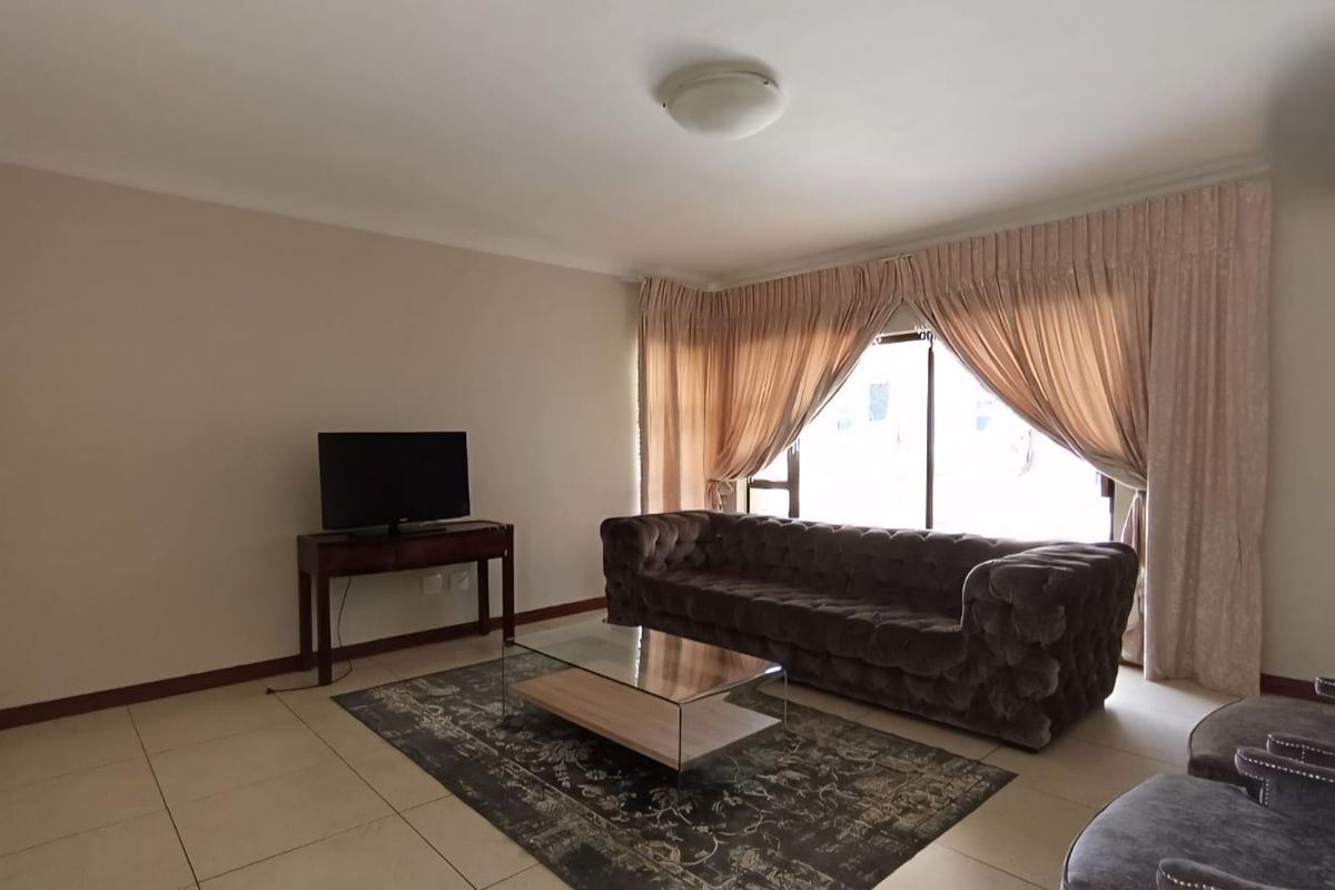 A spacious living room featuring neutral tiled flooring, large windows with draped curtains, and a clean, open layout.