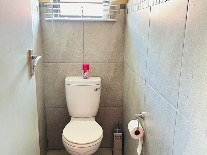 A compact, well-maintained guest bathroom featuring neutral floor-to-ceiling tiling and a window for natural light.