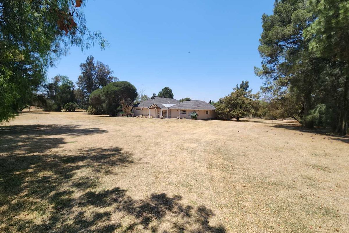 A wide-angle view of the property exterior, showcasing the house set within a large, expansive garden area with mature trees.