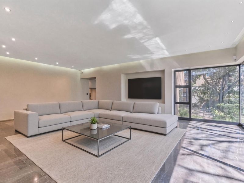 Modern living room featuring large format tiled flooring, recessed ceiling lighting, and expansive floor-to-ceiling glass doors providing natural light and garden views.