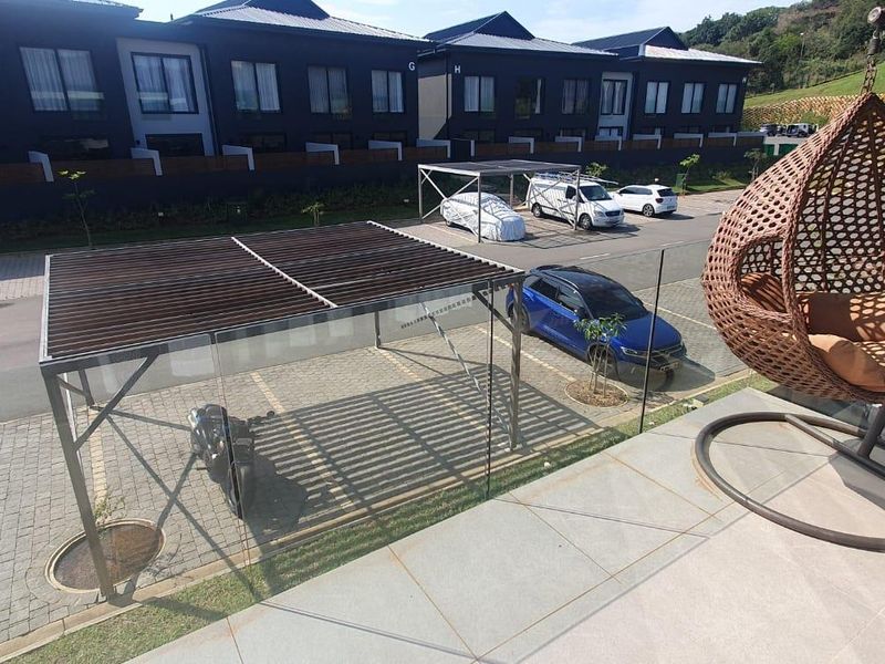 A spacious balcony featuring a glass balustrade and tiled flooring, overlooking a paved parking area and residential complex.