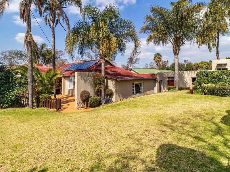 Rear view of the house featuring a spacious lawn, established garden, paved patio area, and roof-mounted solar panels.