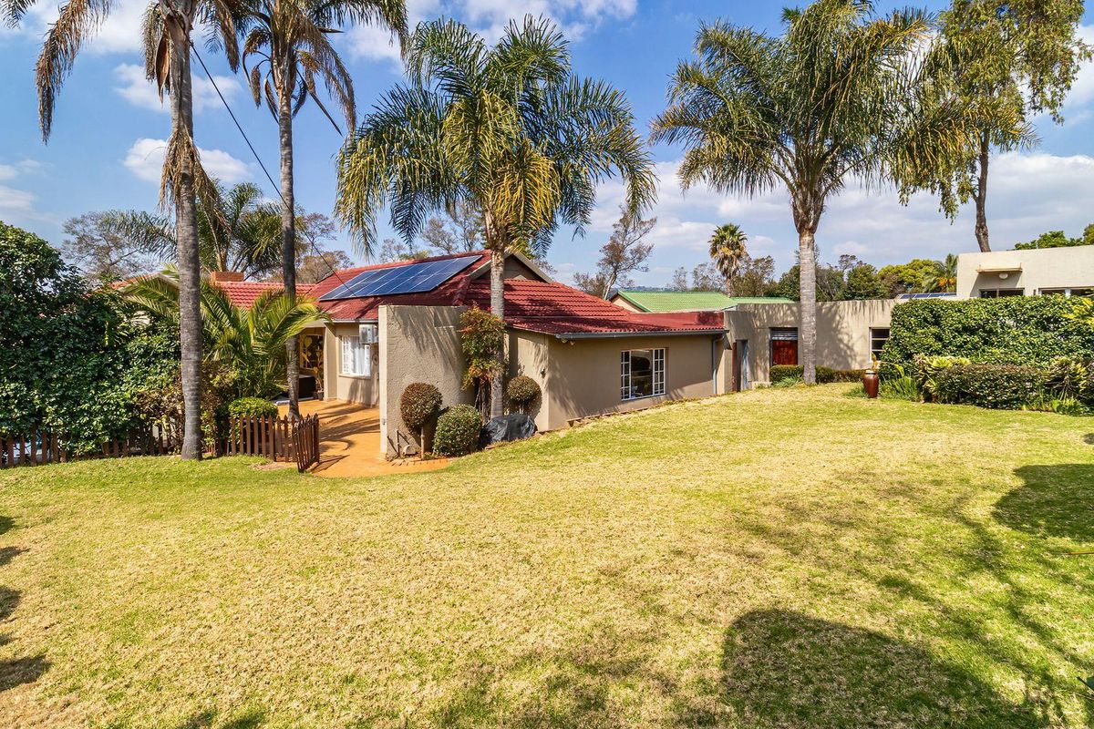 Rear view of the house featuring a spacious lawn, established garden, paved patio area, and roof-mounted solar panels.