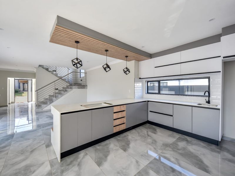 Modern open-plan kitchen featuring sleek grey and white cabinetry, quartz countertops, a timber ceiling detail, and polished porcelain flooring, seamlessly connected to the staircase area.