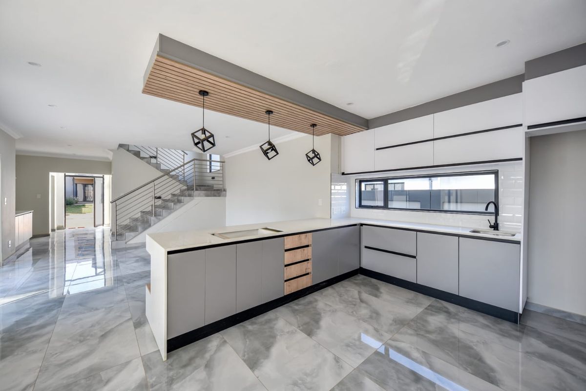 Modern open-plan kitchen featuring sleek grey and white cabinetry, quartz countertops, a timber ceiling detail, and polished porcelain flooring, seamlessly connected to the staircase area.