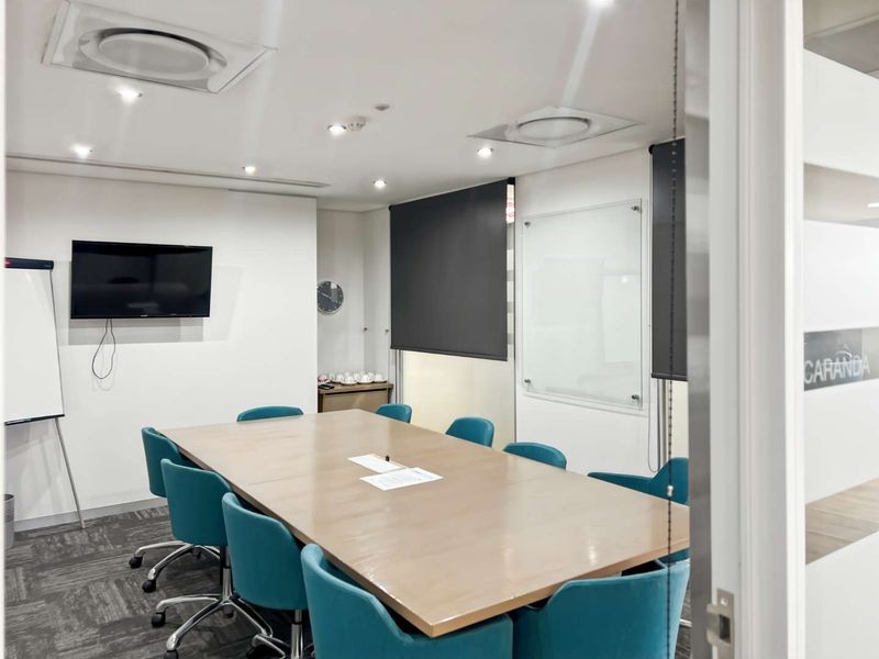 A professional office meeting room featuring a large conference table, glass whiteboard, recessed ceiling lighting, and integrated air conditioning vents.