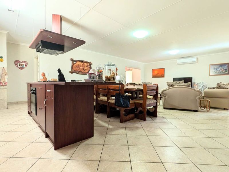 Spacious open-plan living area featuring a central kitchen island with built-in oven, extractor fan, and neutral ceramic tile flooring throughout.
