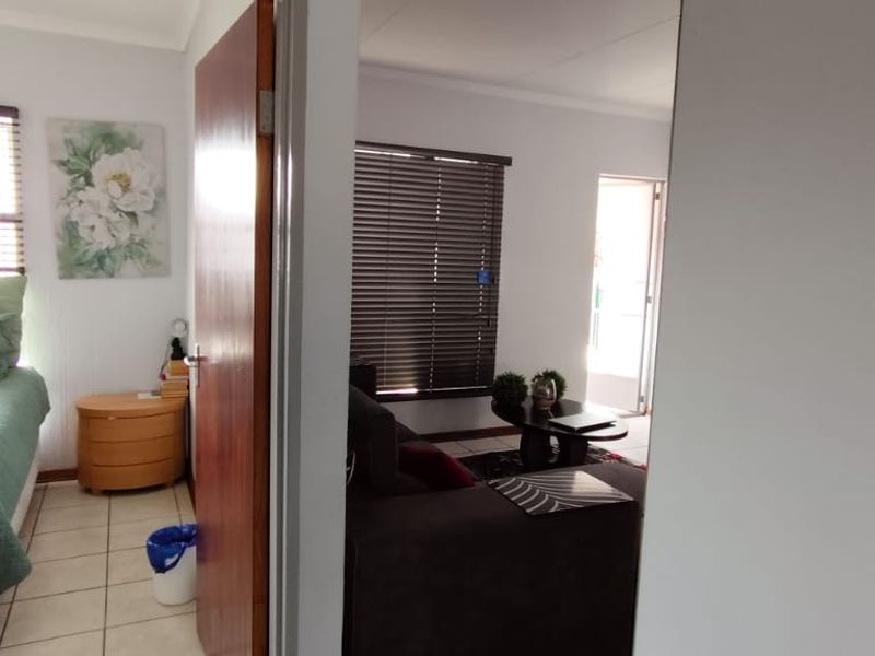 A view from a hallway looking into a bedroom and a living area, featuring tiled floors and venetian blinds.