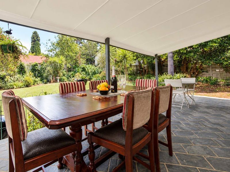 A spacious covered patio featuring slate tile flooring, overlooking a lush, well-maintained garden area.