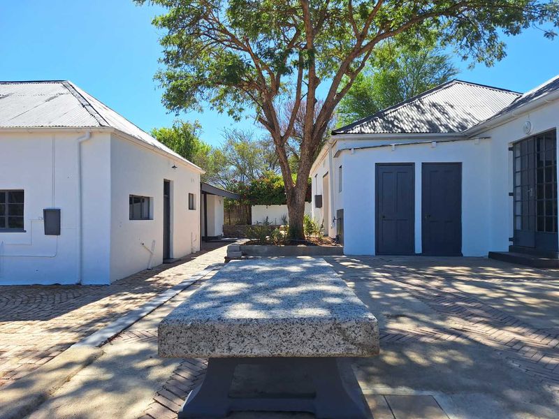 A well-maintained courtyard area between guest house buildings, featuring paved surfaces, a stone bench, and mature trees.