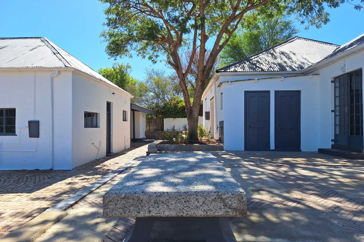 A well-maintained courtyard area between guest house buildings, featuring paved surfaces, a stone bench, and mature trees.