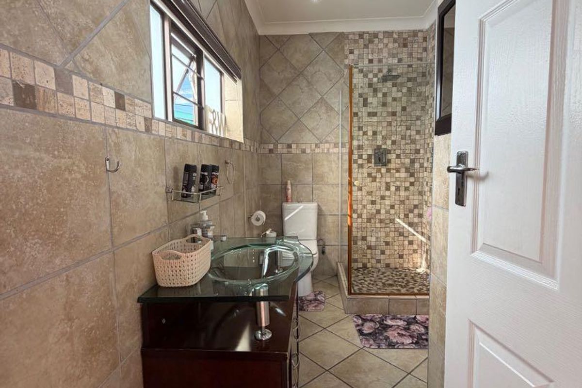 A functional bathroom featuring a glass vessel sink vanity, a walk-in shower with mosaic tile accents, and neutral floor-to-ceiling wall tiling.