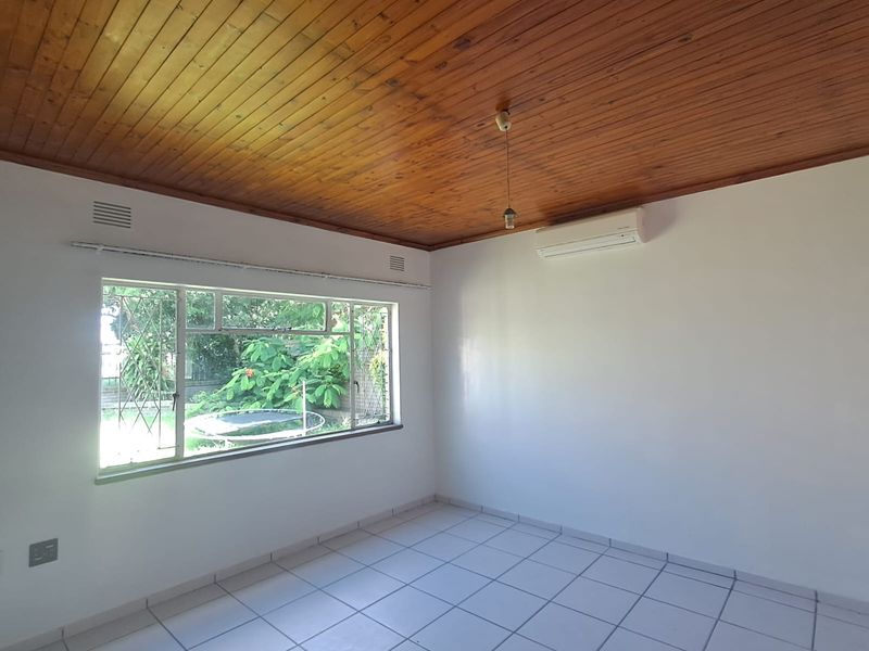 A bright, empty bedroom featuring a warm timber ceiling, tiled flooring, and a wall-mounted split-system air conditioner.